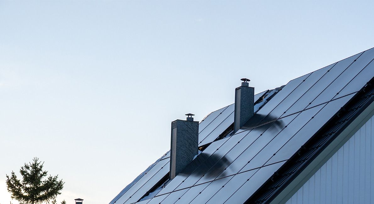 Svarta solpaneler på ett sadeltak med två skorstenar, mot en ljus himmel