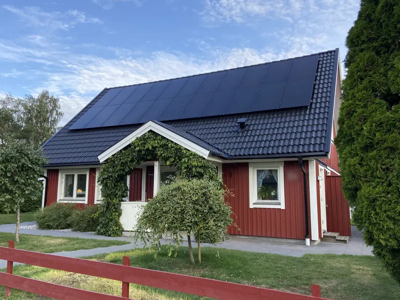 Rött trähus med helsvarta solcellspaneler på det mörka tegeltaket en solig sommardag