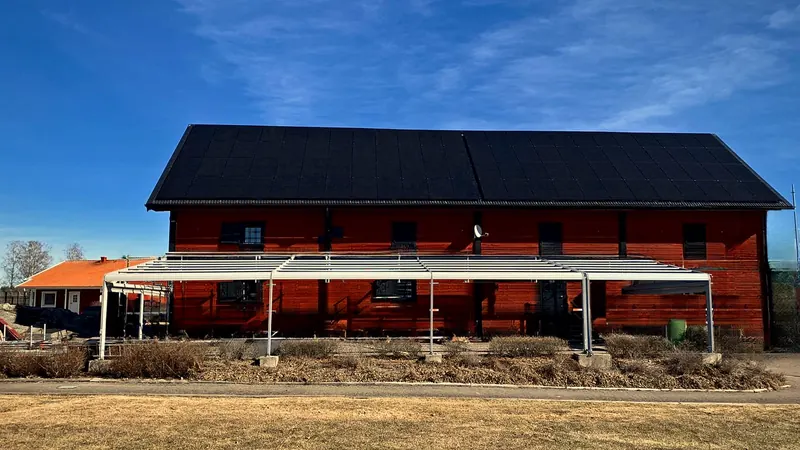 Solceller på Vreta Kloster Golfklubbs röda träbyggnad – svarta solcellsmoduler över hela taksidan